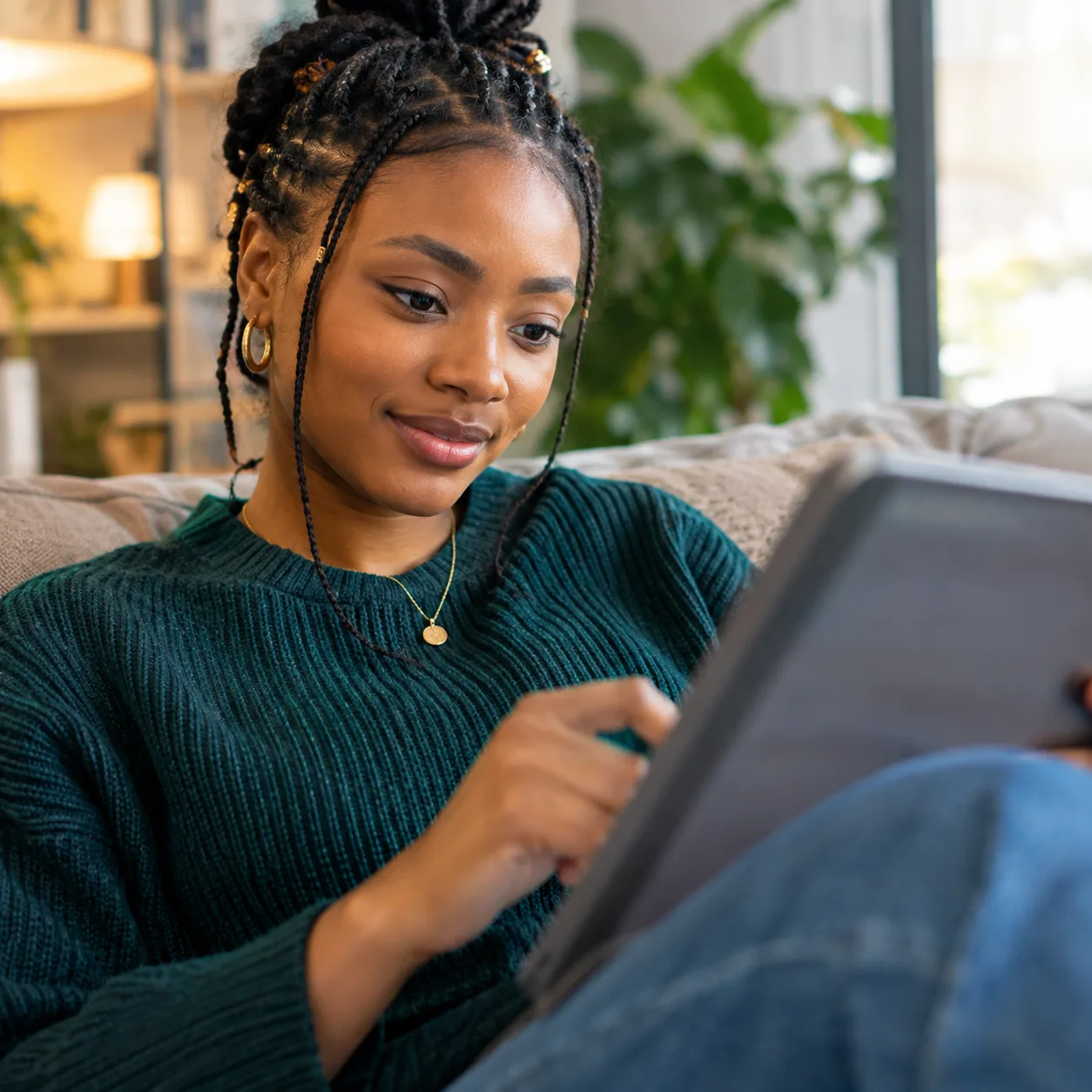 Une jeune femme suit son parcours de formation sur une tablette, installée dans son canapé